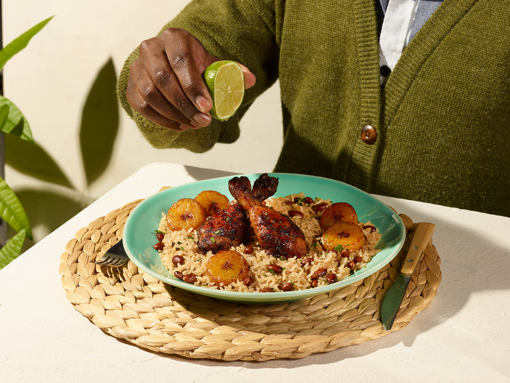 Un homme presse un quartier de lime au-dessus d'un plat de poulet jerk avec riz