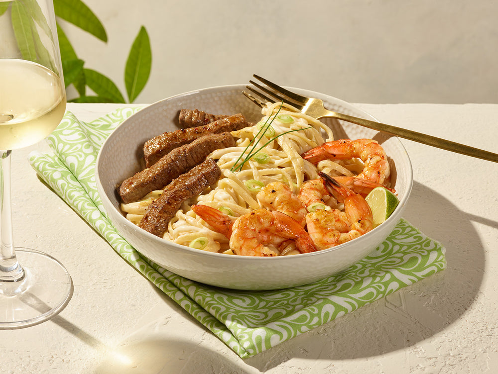 Plat de linguine avec crevette et boeuf posé sur un linge avec verre de vin blanc