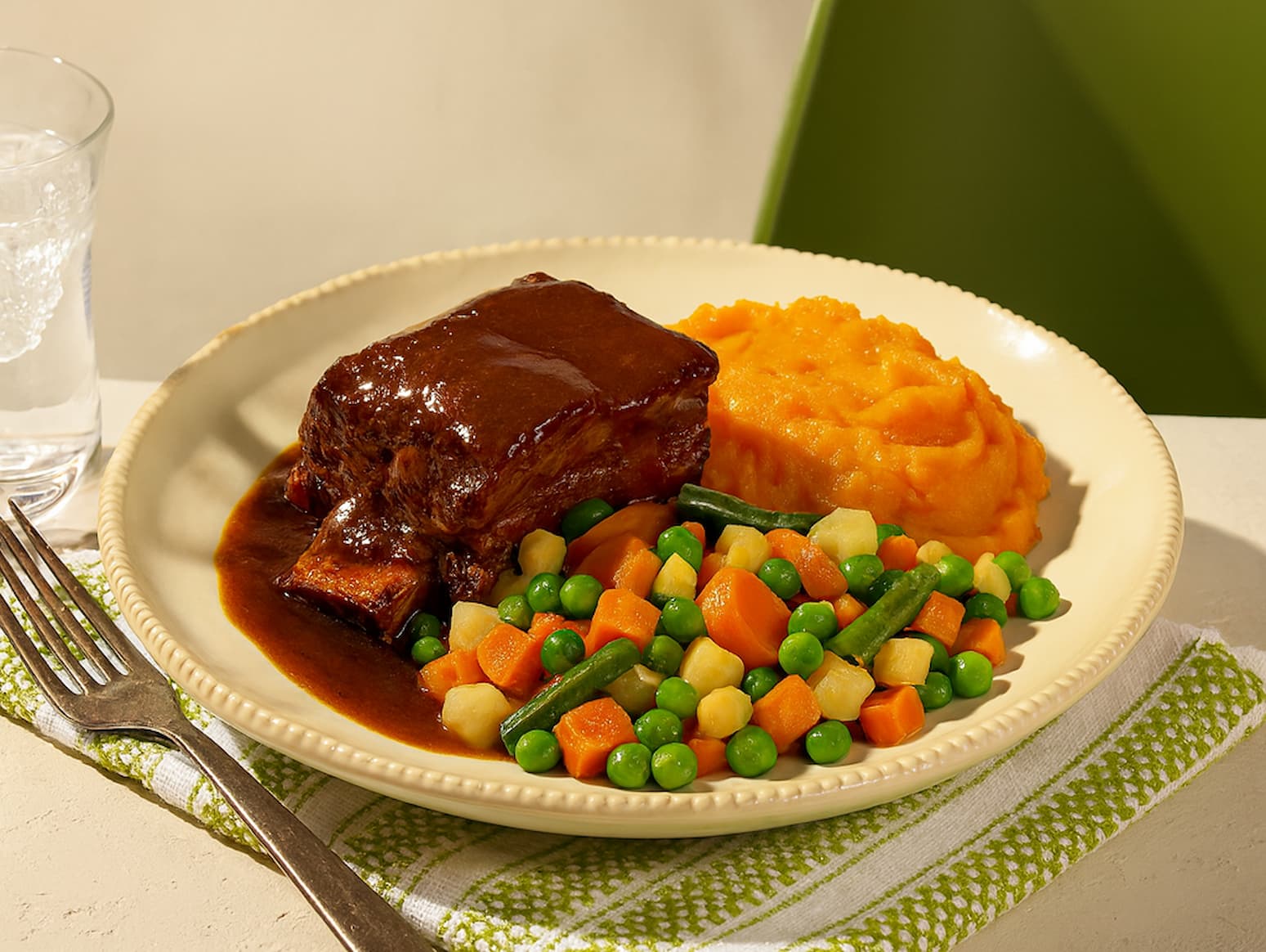 Assiette remplie de légumes, de purée et de viande en sauce. 
